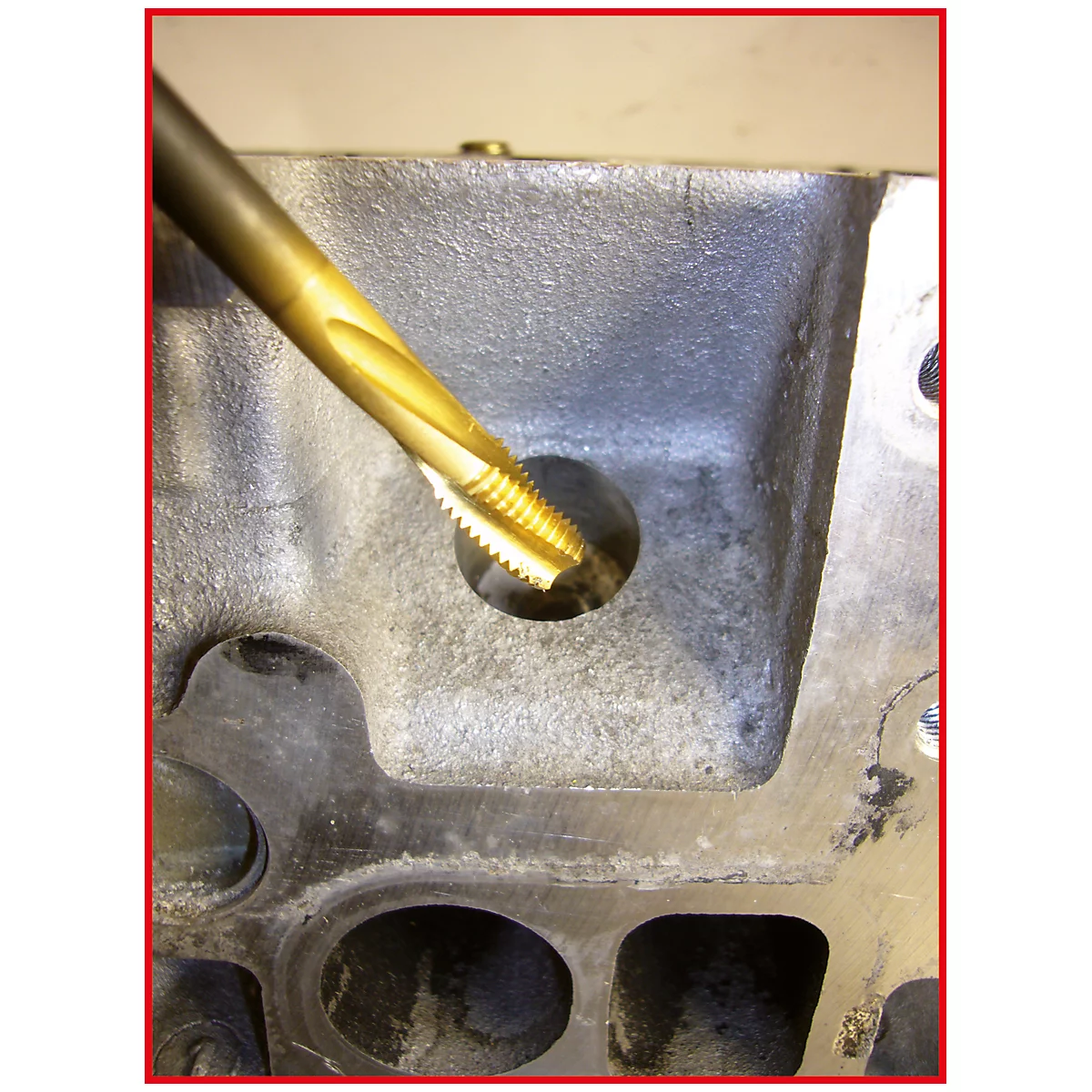 Nahaufnahme eines metallischen Lochs, das mit einem goldfarbenen Gewindeschneider bearbeitet wird.